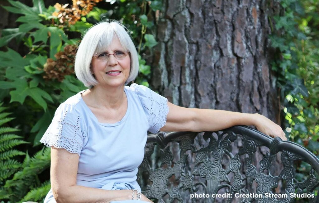 Headshot of C Hayes sitting on a bench in front of a tree