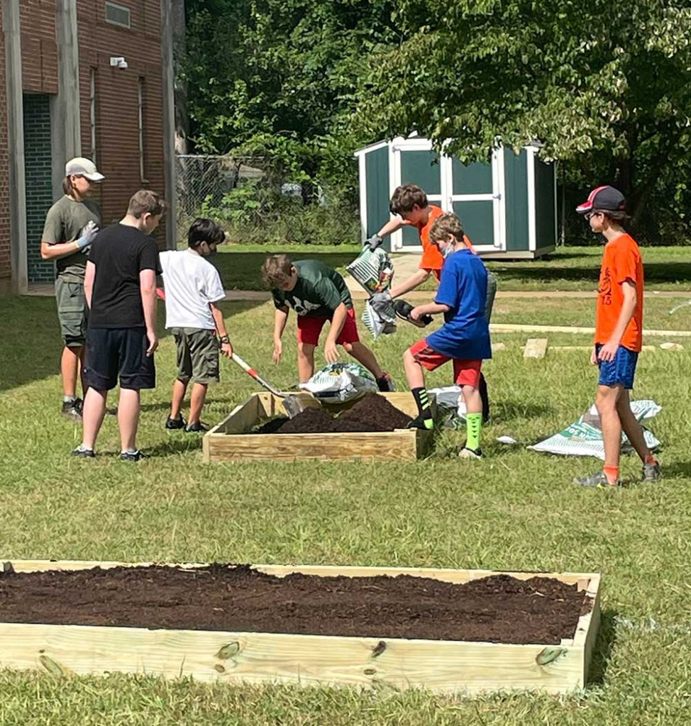 Students fill a recently created raised bed with dirt with a complete raised bed in the foreground