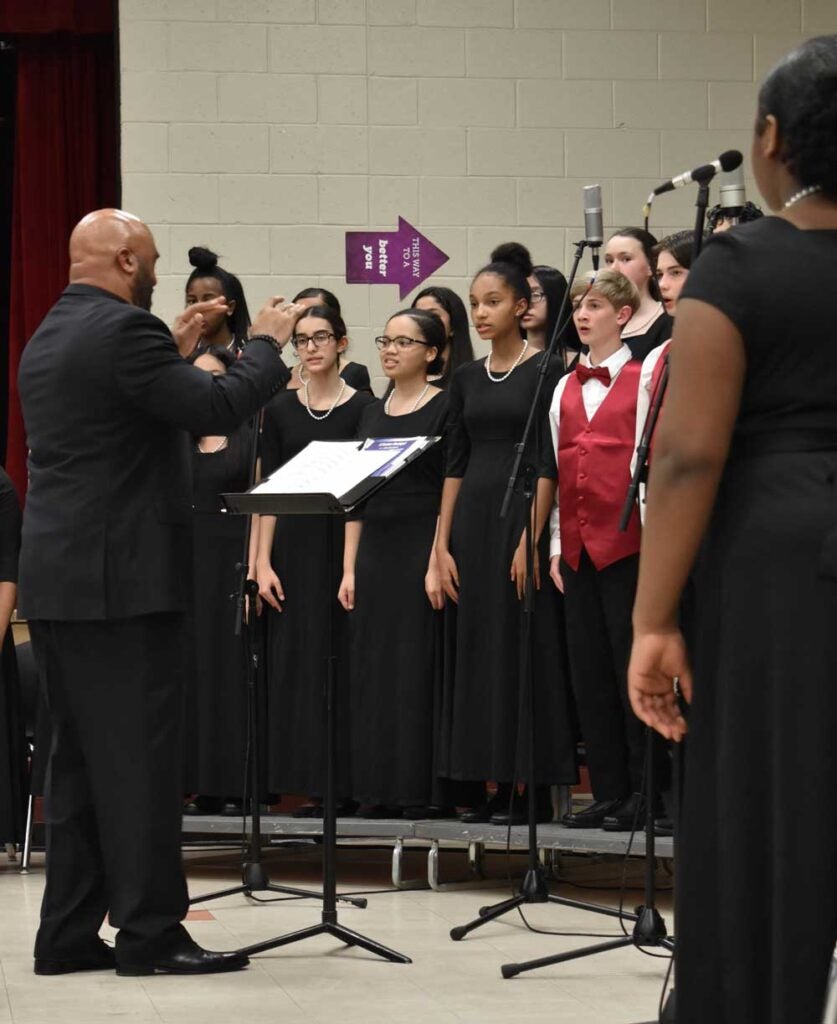 Youth choir practicing in formal dress, the conductor's back is to us