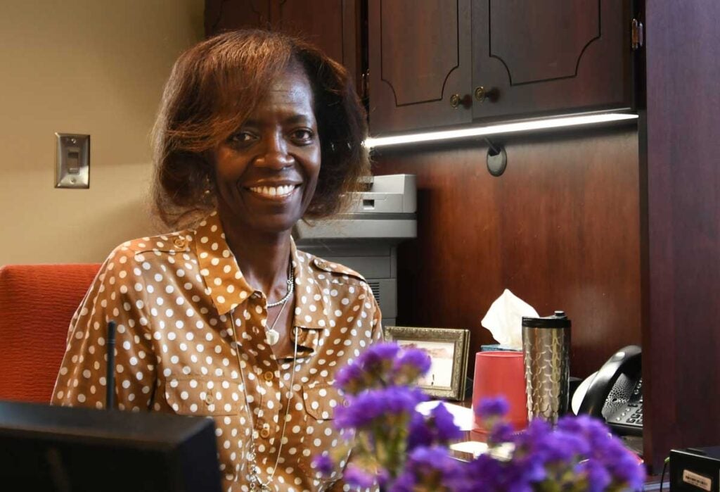 Doctor Satterfield in her office with purple flowers in the foreground and phone and copy machine in the back