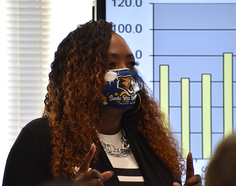 P McCloud's head and shoulders as she speaks in front of a large projection of an info graphic