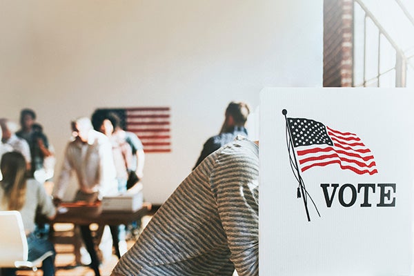 Person in foregrounds leans into private voting booth while people in background wait