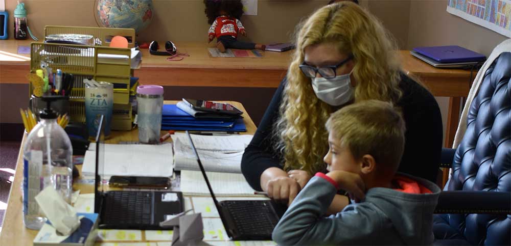 Woman helps boy at with laptop