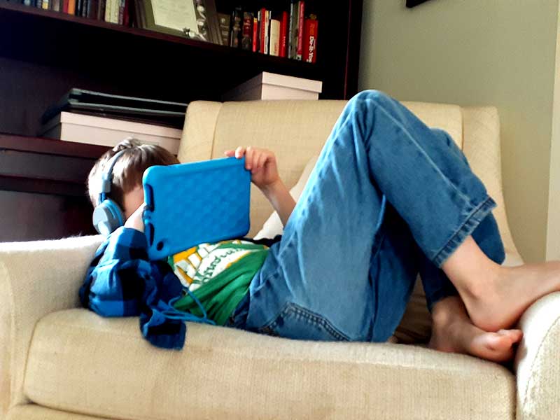 A boy with headphones on a tablet lays on a couch