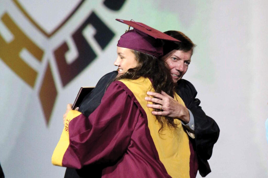 Adult in suit embraces student in graduation garb