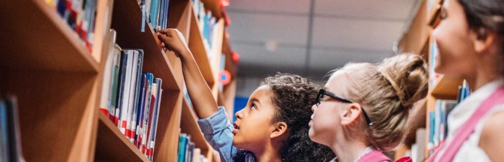 Children picking books off of a library bookshelf